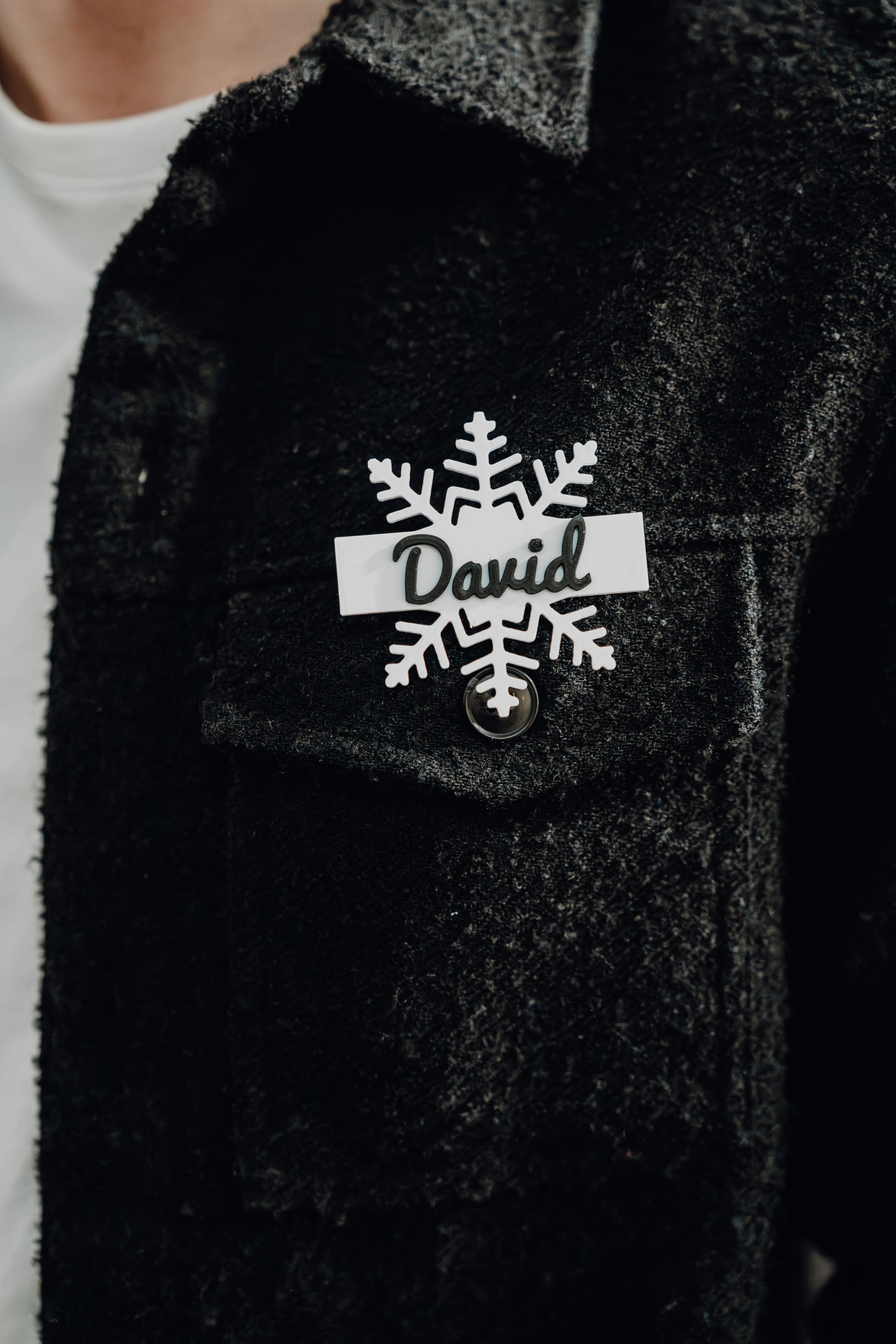 Schwarz-weißes personalisiertes Namensschild in Schneeflockenform mit dem Namen David auf einem schwarzen Blazer.